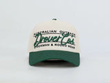 A two-tone baseball cap with an off-white crown and a dark green brim, featuring green and black embroidered text that reads 'AUSTRALIAN OUTBACK Drovers Co STOCKMAN & RODEO WEAR'.