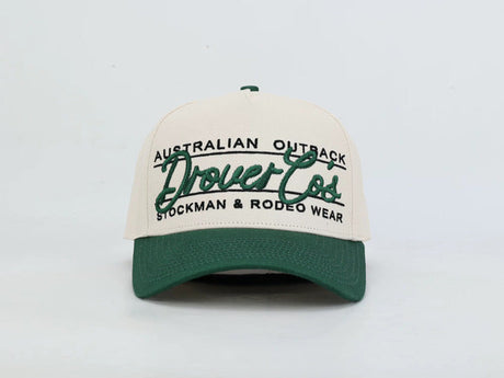 A two-tone baseball cap with an off-white crown and a dark green brim, featuring green and black embroidered text that reads 'AUSTRALIAN OUTBACK Drovers Co STOCKMAN & RODEO WEAR'.